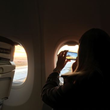Person looks out airplane window with phone in hand.